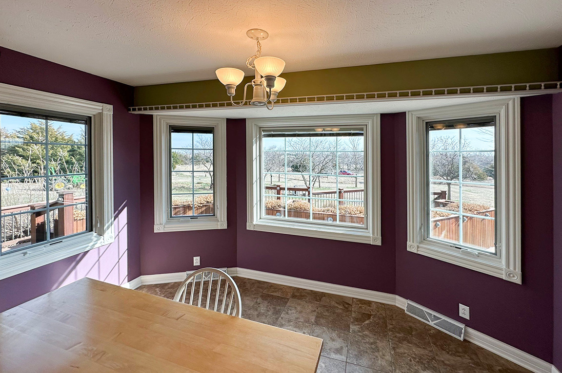 A modern kitchen with purple walls and multiple replacement windows, featuring a wooden table and natural light.