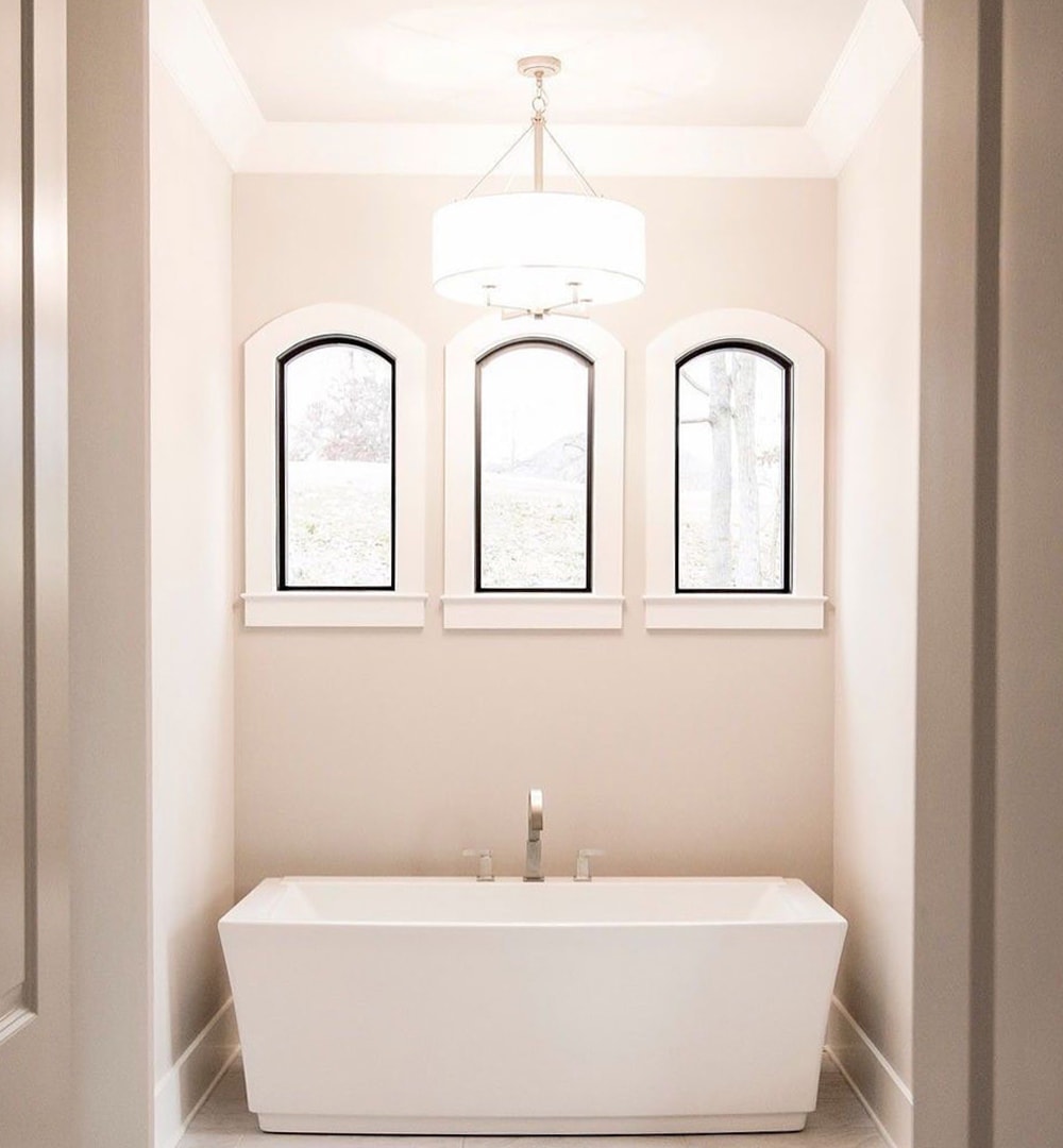 Black picture windows with white trim placed above rectangular white tub in bathroom nook.