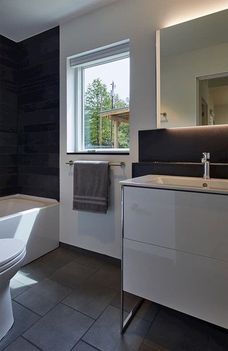 Modern bathroom with dark floor and shower wall and white window and vanity