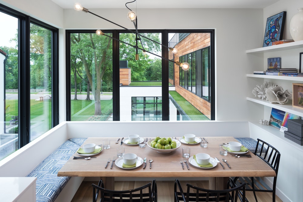White dining room nook with benches around the table and tall black casement windows