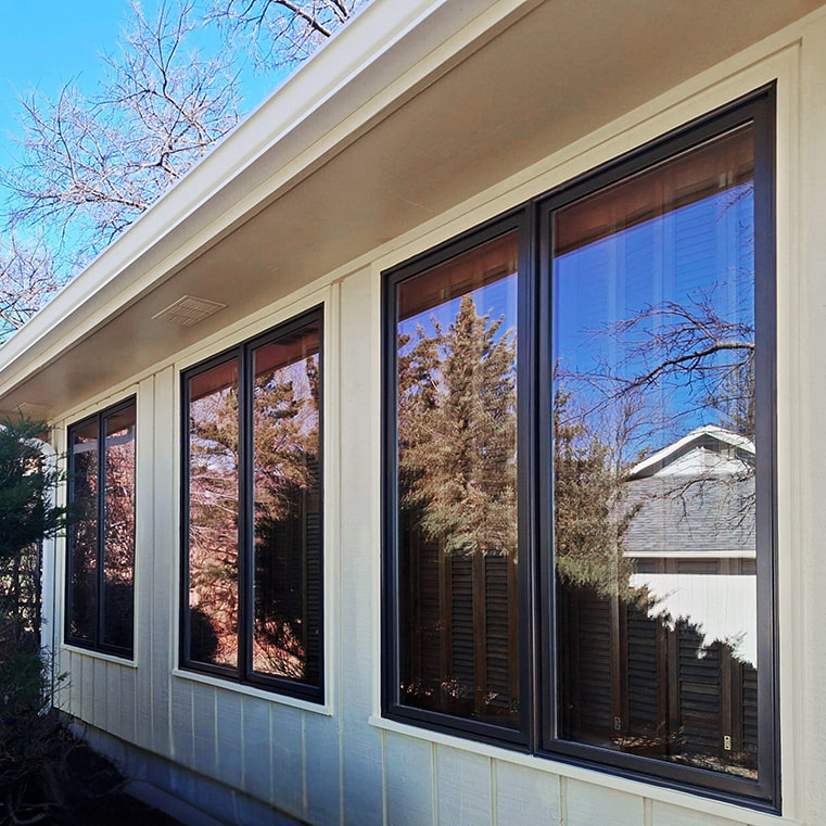A modern yellow sunroom featuring large windows with black frames, surrounded by greenery.