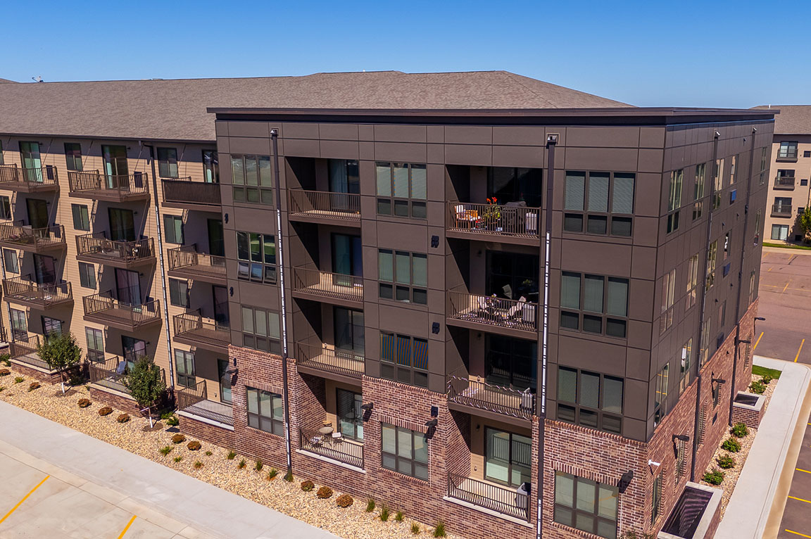 A modern apartment building with large apartment windows and balconies overlooking a parking lot.