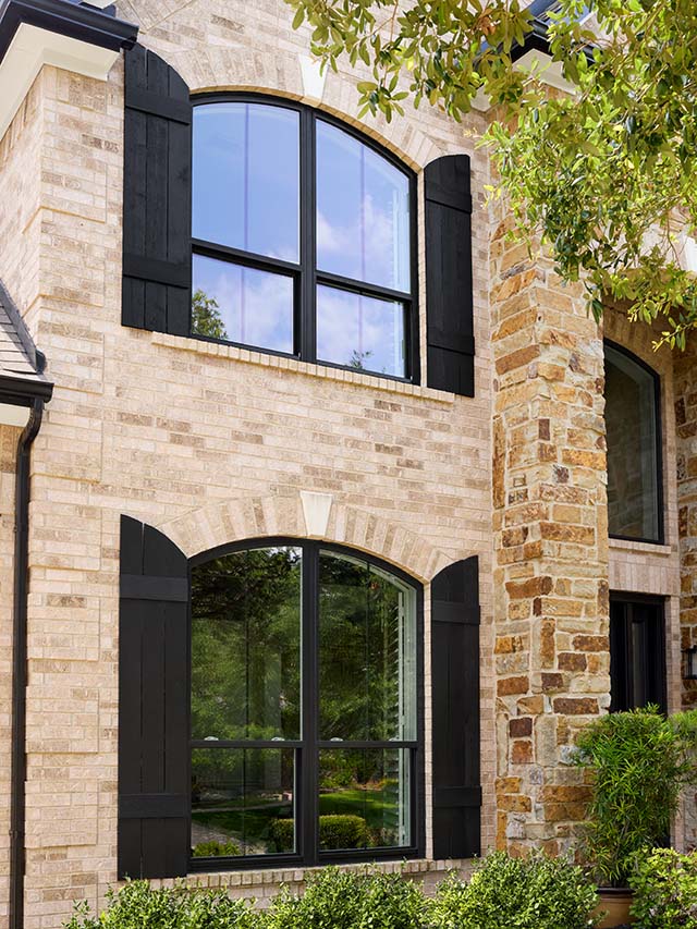 Black framed arched windows on brick and stone home exterior.