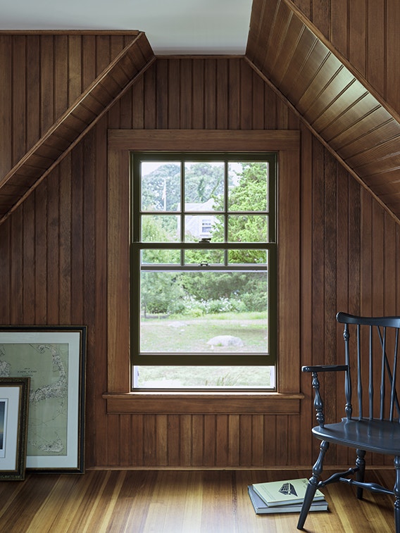 A cozy room featuring dark wood paneling and a classic interior window trim, with a view of greenery outside.