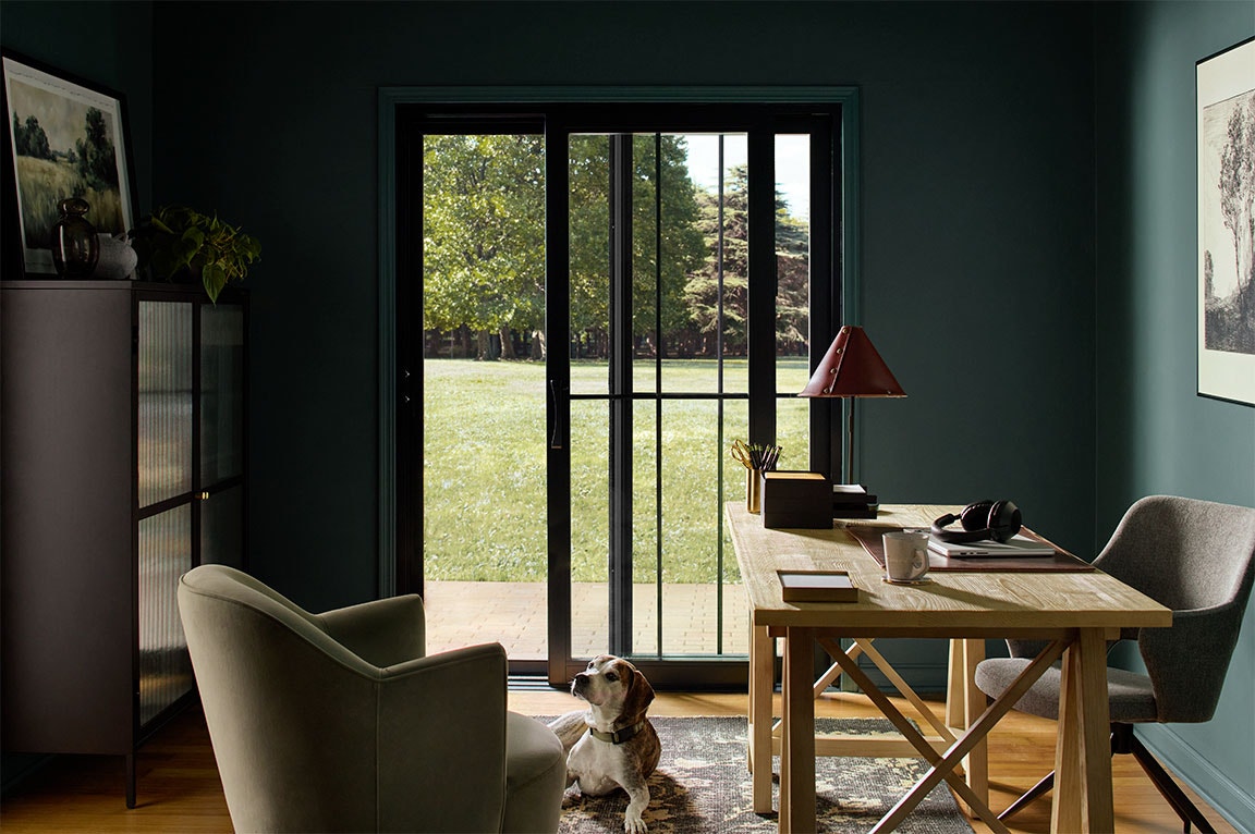 Black sliding patio door is open, bringing fresh air and natural light into a dark home office.