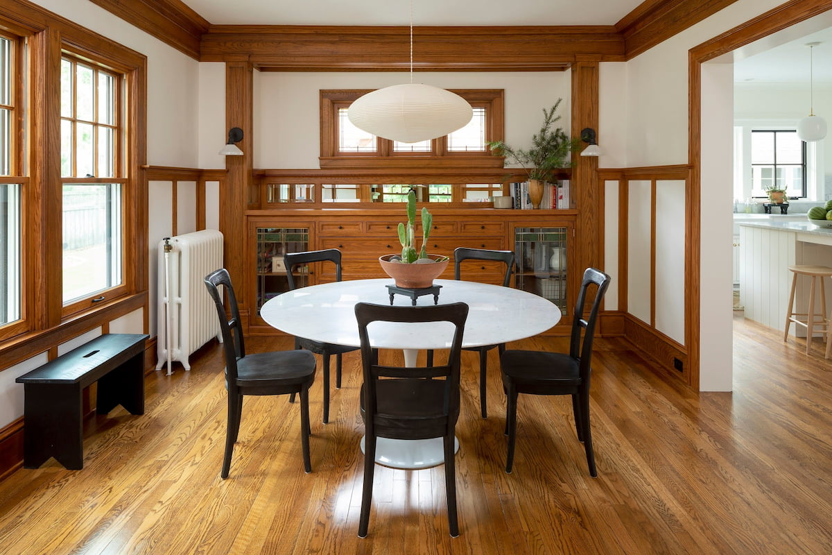 A dining room has a round table surrounded by wood built-ins and craftsman windows with grilles.