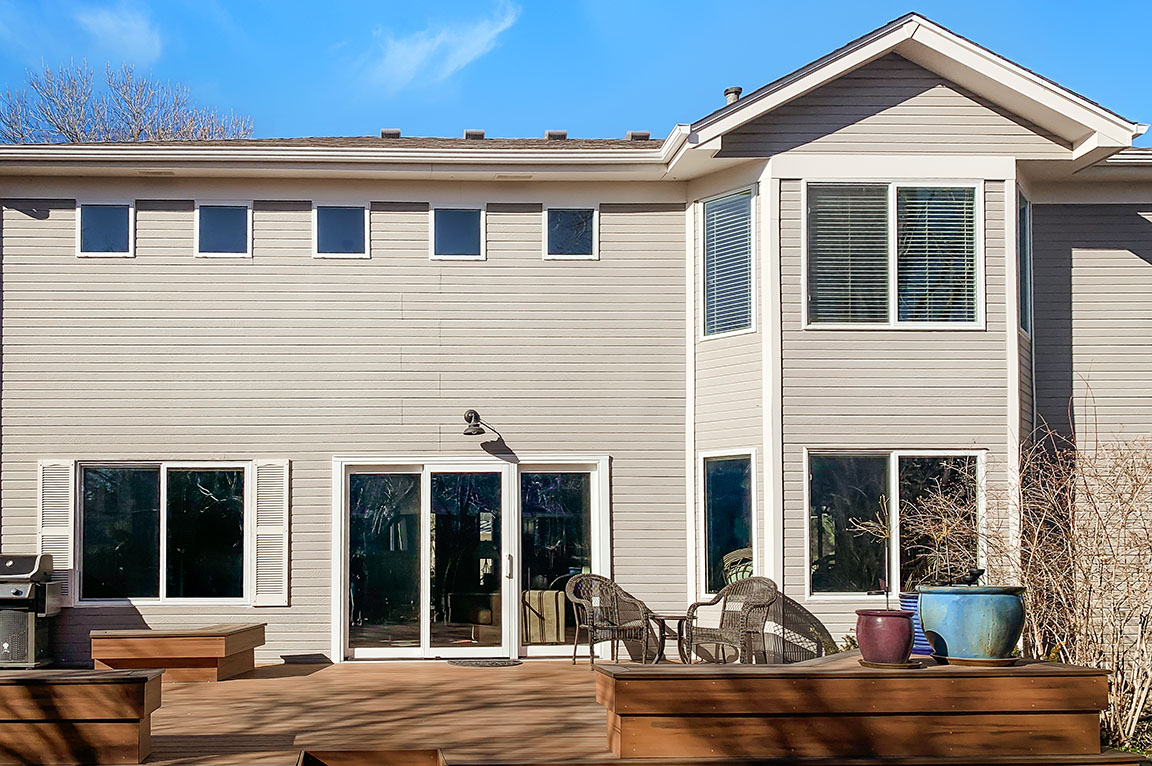 Rear exterior of two‑story home with wood deck, sliding glass doors, and large windows.