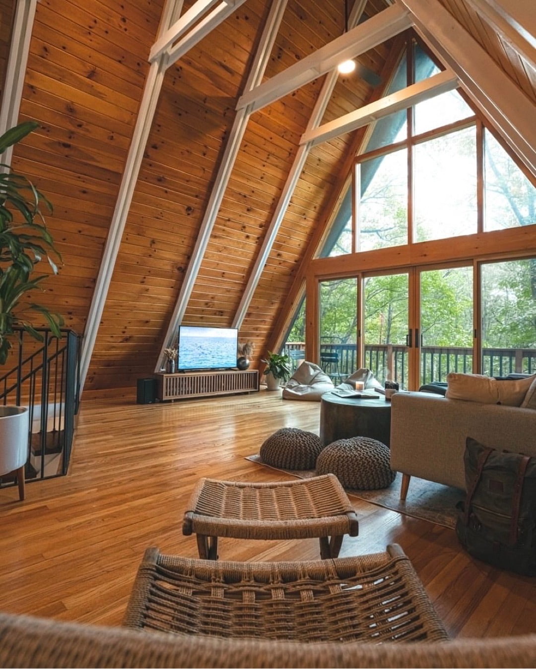 A window wall with triangle windows and a sliding door sits within a wood A-frame living room.