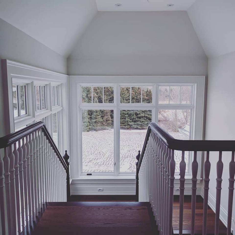 looking down at the top of the stairs to the landing with white casement windows bringing in light