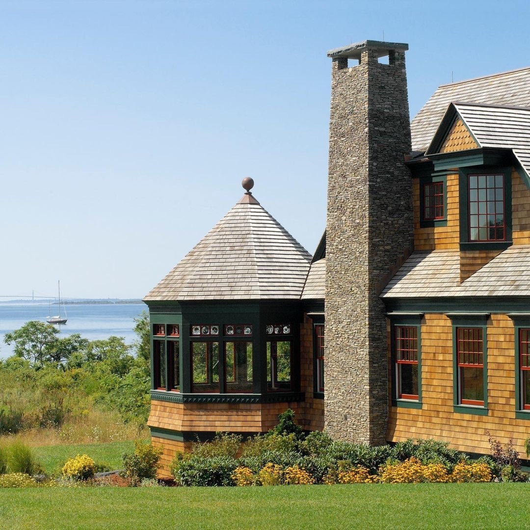 The exterior of a coastal home has wood shake siding, red windows and green trim.