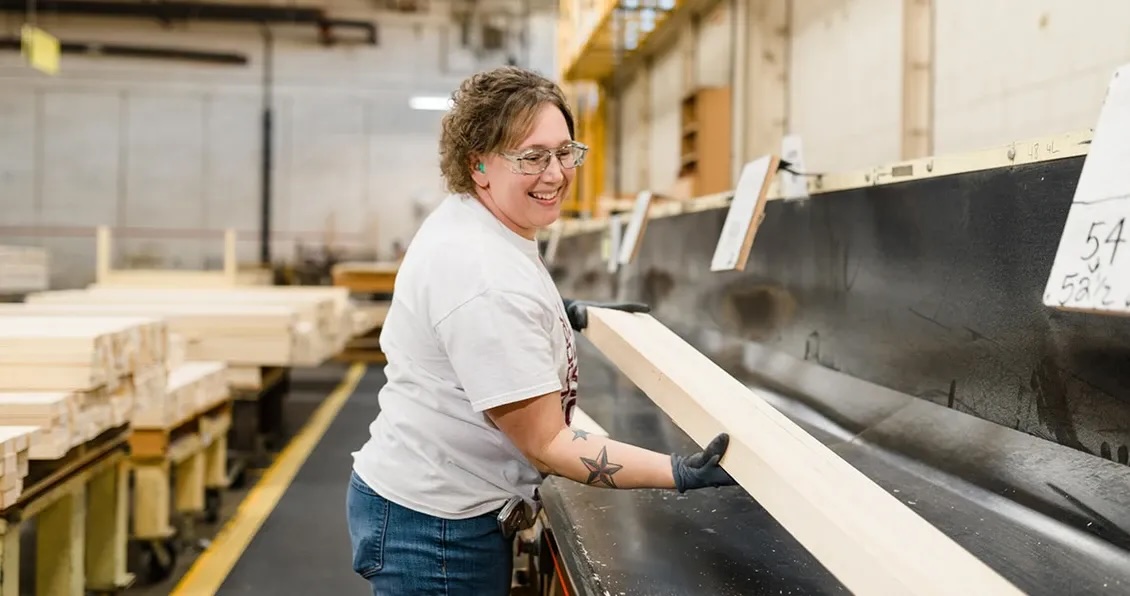 Smiling worker handling wood planks in a factory setting, showcasing careers in manufacturing.