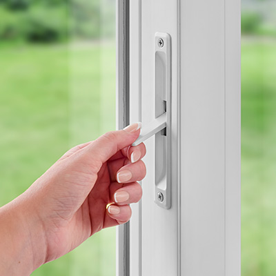 Hand engaging secondary window lock on white vinyl window.