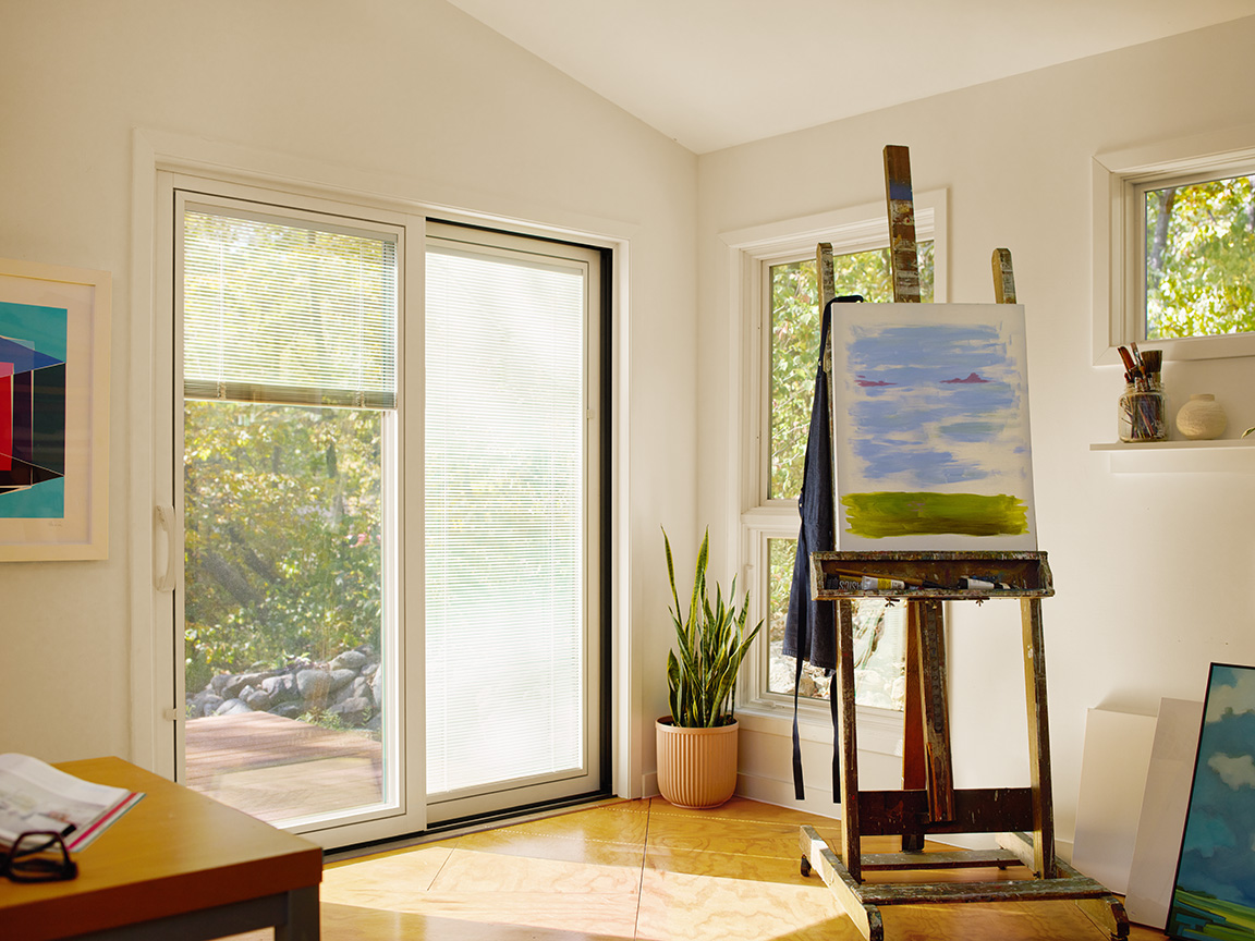 Tan sliding patio doors with blinds-between-the-glass bring sunlight into an art room.