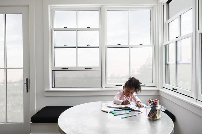 Little girl sitting at a table in a room with white windows and doors and an open window featuring a retractable screen