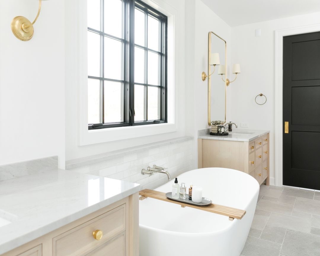 Black casement windows sit behind a white freestanding bathtub in this clean and bright bathroom.