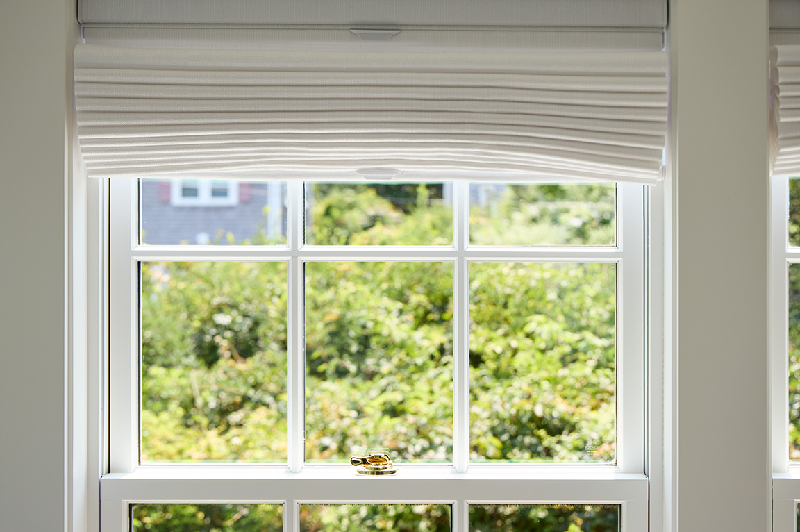 A view of traditional windows with grilles, featuring white blinds and a lush green landscape outside. 