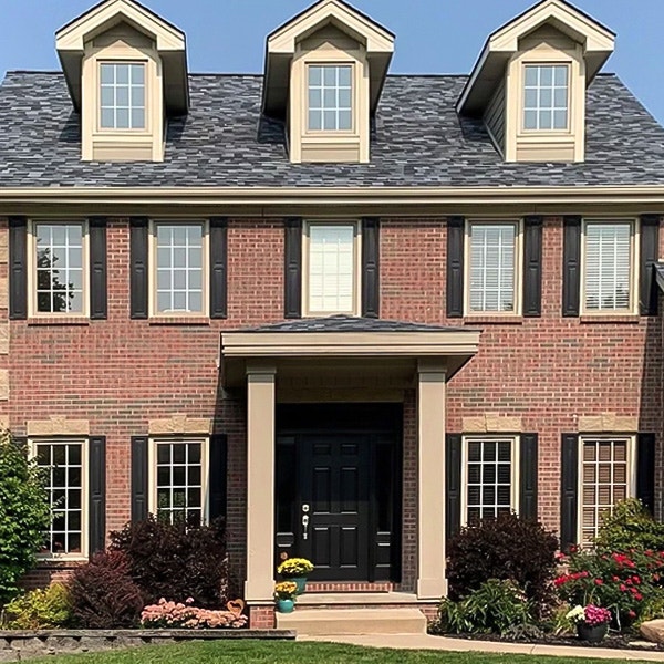 A colonial brick home with tan windows and black shutters.