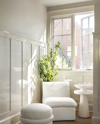 a mono-chromatic sitting area featuring a chair, footstool, plant and two casement windows open to let in the fresh air.