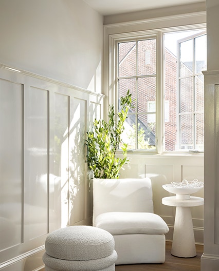 a mono-chromatic sitting area featuring a chair, footstool, plant and two casement windows open to let in the fresh air.