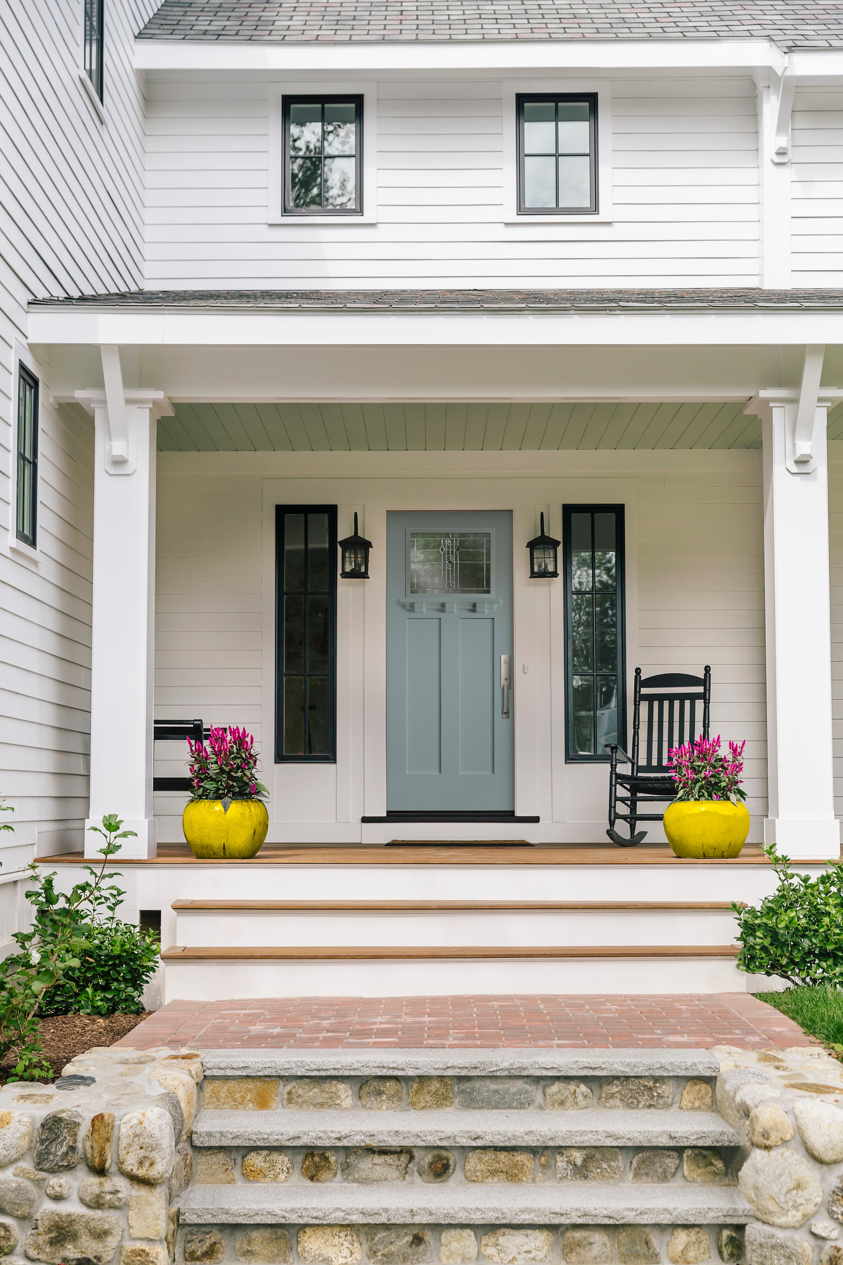 Blue craftsman front door with decorative glass and modern hardware surrounded by black windows on white house