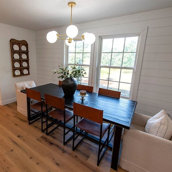 a dark wood dining room table in front of two white double-hung windows