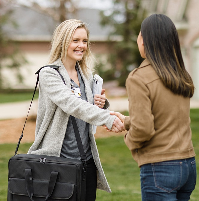 Two women shaking hands outdoors in Harrisburg, one holding a black bag and documents.