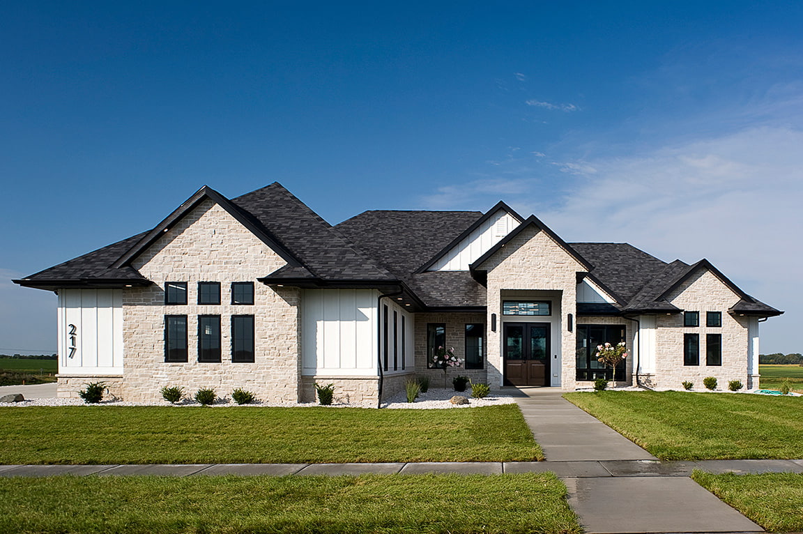 A modern home exterior with stone siding and new construction windows, showcasing a well-manicured lawn.
