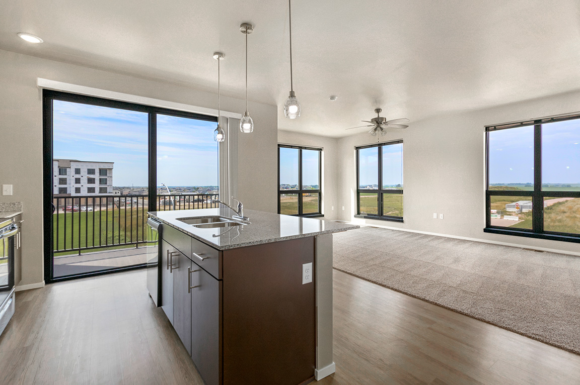 Spacious apartment with large floor-to-ceiling windows overlooking grassy fields and a balcony.