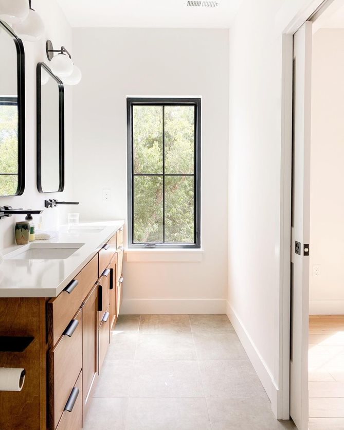 A black farmhouse window with simple grilles on a white wall at the end of a bathroom.
