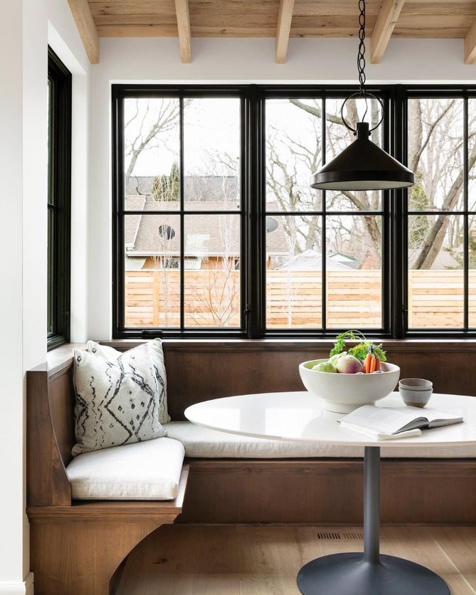 Black casement windows with traditional grille patterns behind a dining room breakfast nook.