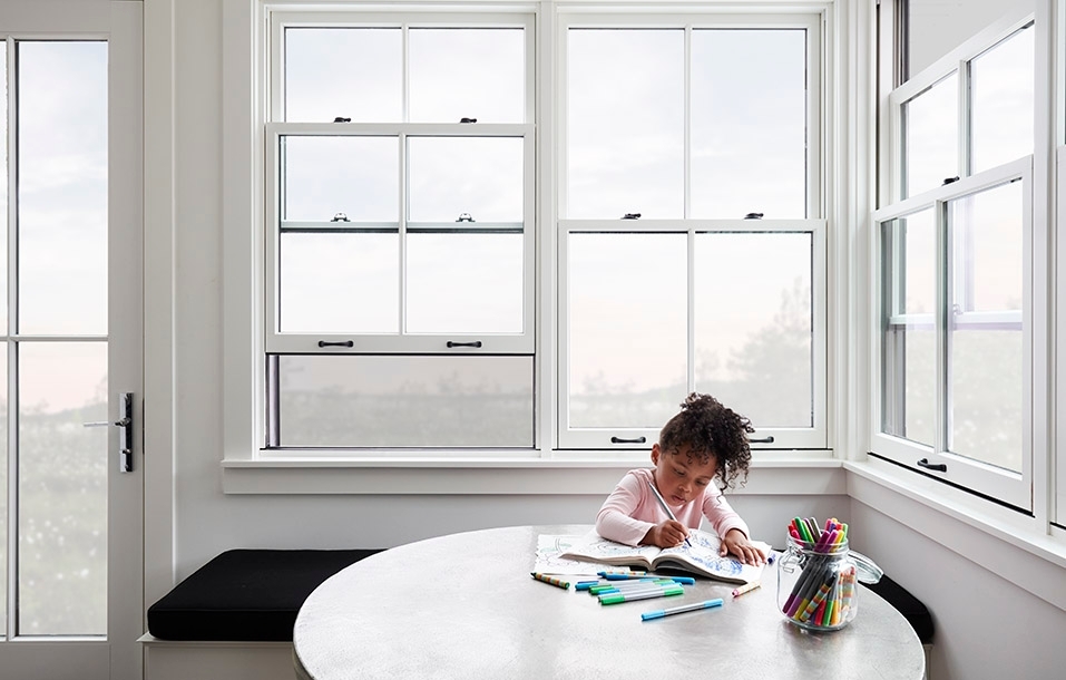 small child colors at a table in front of pella windows