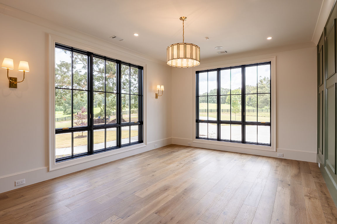 Spacious living room featuring large windows, hardwood flooring, and elegant lighting fixtures.