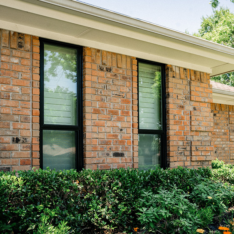 A brick home with two black windows, surrounded by shrubbery. 