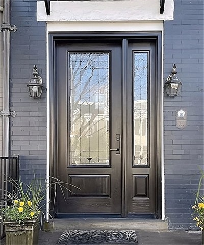An entryway has a black front door with decorative glass and a sidelight on the right side. 