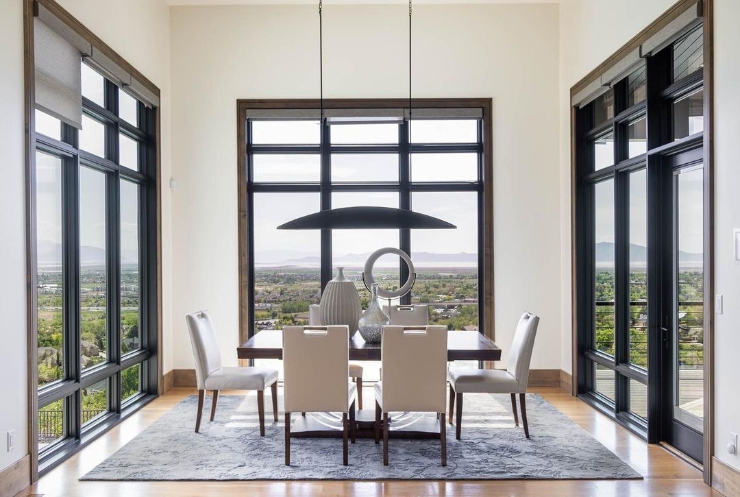 A modern-style dining room features large black picture windows and a hinged patio door.