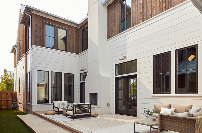 an outdoor patio sits in the corner of a new home with black doors and windows