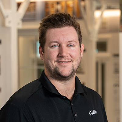 A man with a small goatee is wearing a black Pella shirt