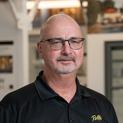 An older man with a gray beard and glasses is wearing a black Pella shirt.