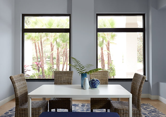 two large fixed windows behind a dining room table in a tropical region