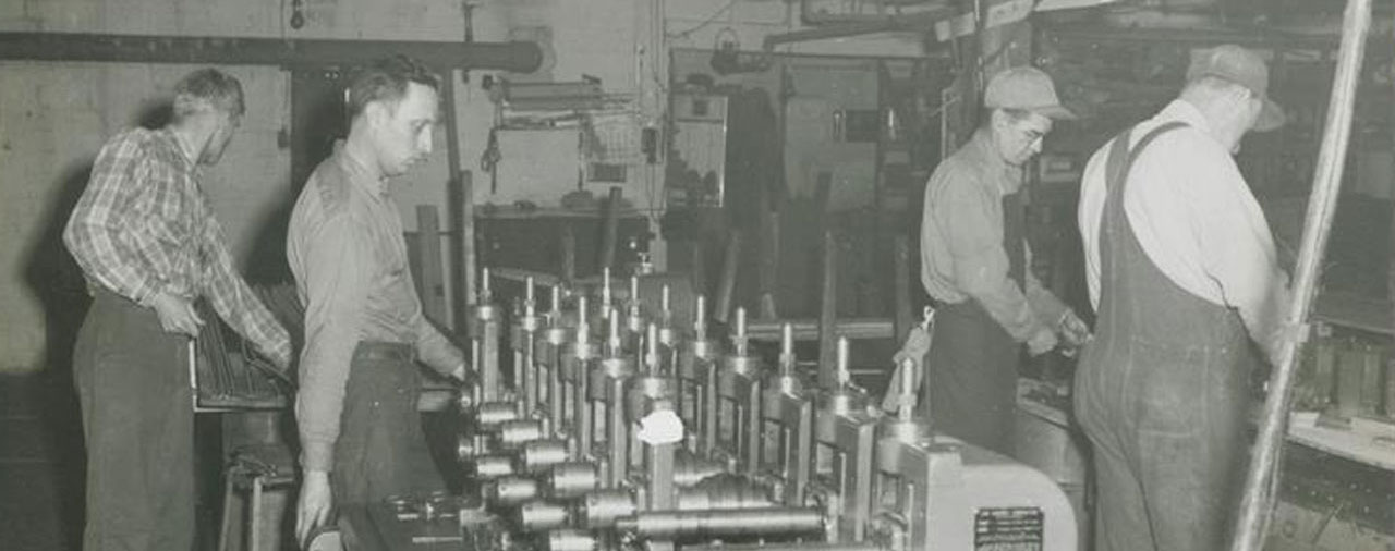 an old black-and-white photo of four men working in a manufacturing plant. 