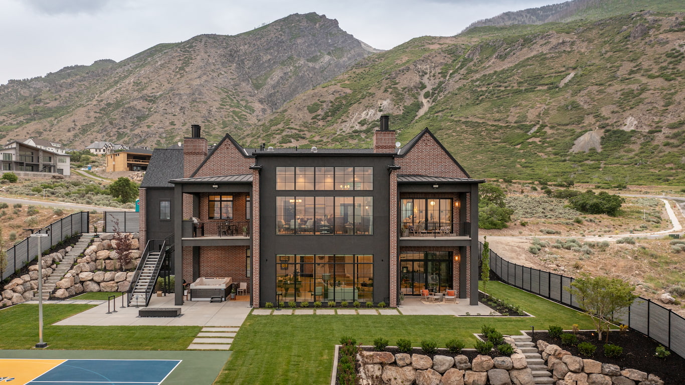 The exterior of a traditional home near the mountains features black windows and doors and a big backyard.
