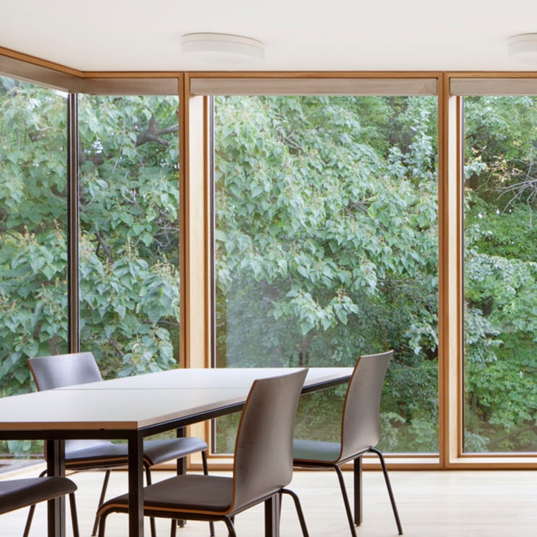 Modern kitchen with floor-to-ceiling windows, wooden frames, and a dining table overlooking lush greenery.