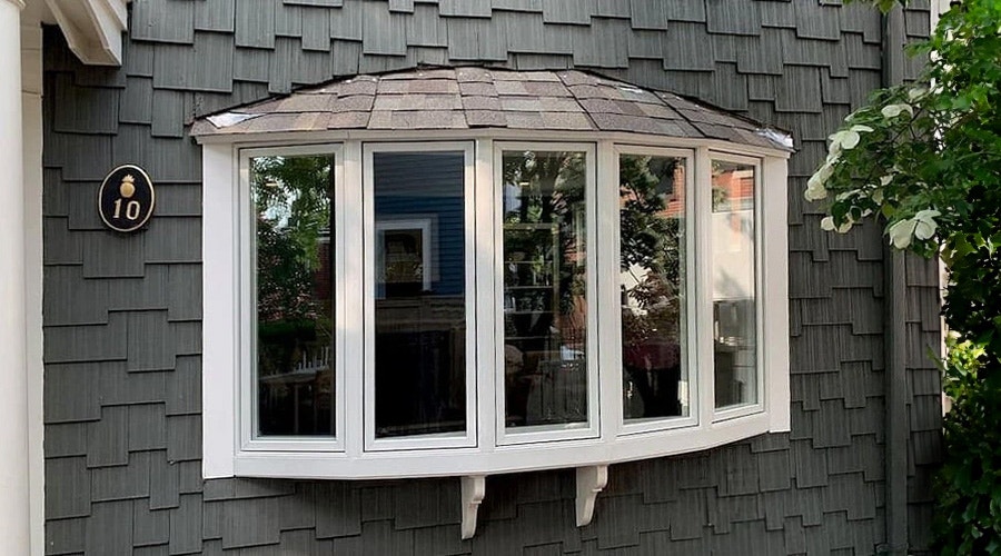 A bow window replacement with white trim on a house featuring shingle siding.