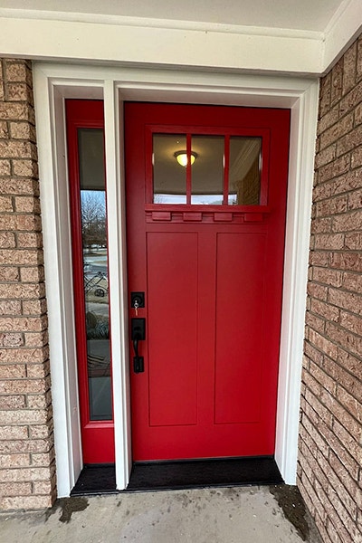 A brand new Red Pella Front entry door with a red full light sidelight on a brick home exterior