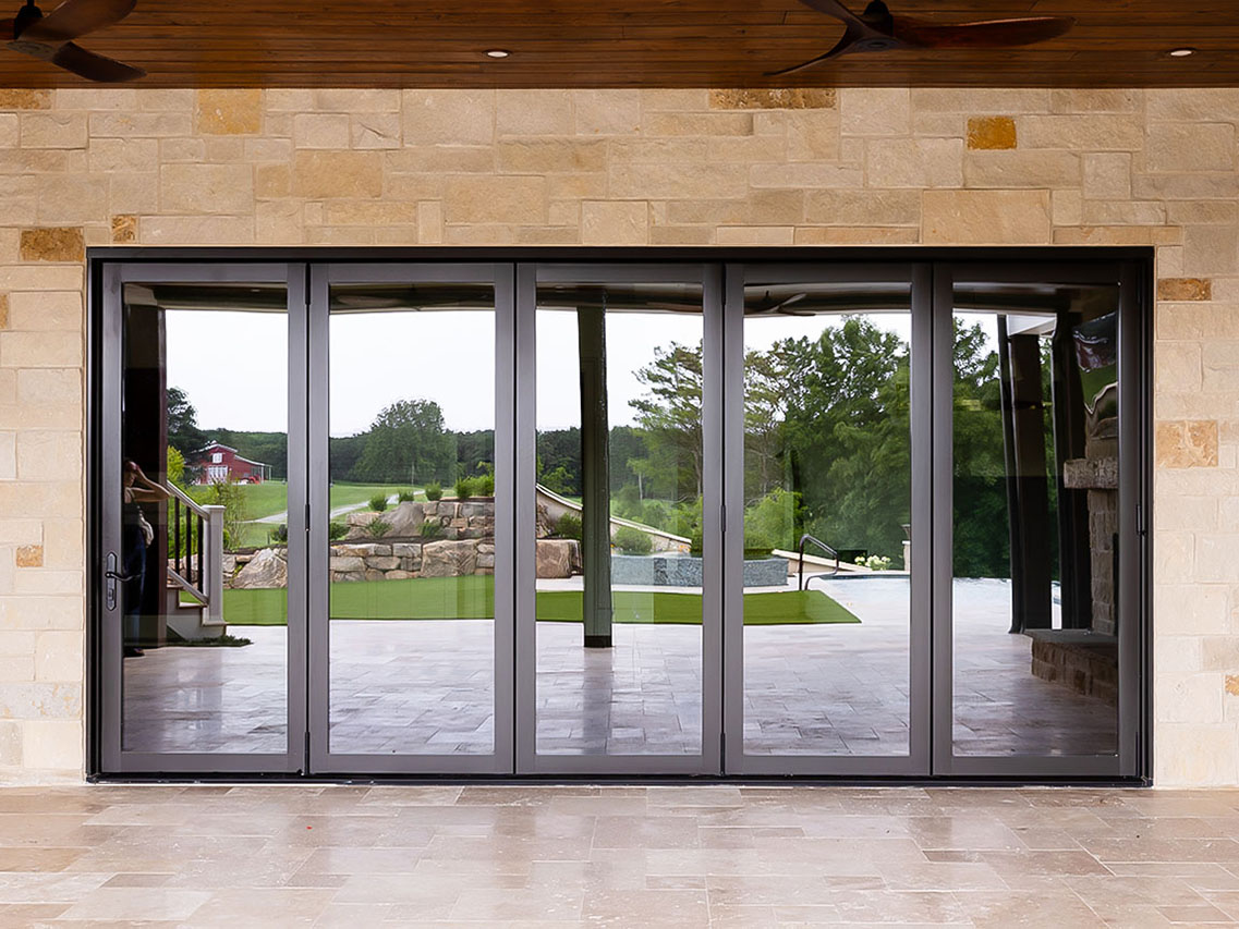 Closed folding glass doors providing a view of an outdoor garden area with lush greenery and stone features.