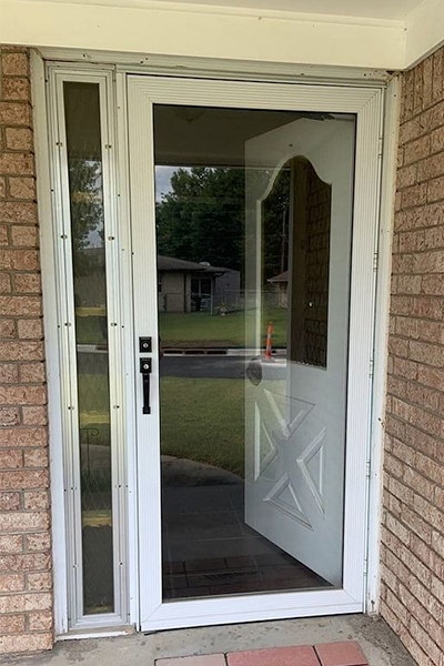 an old white front door with a full light storm door on a brick home exterior