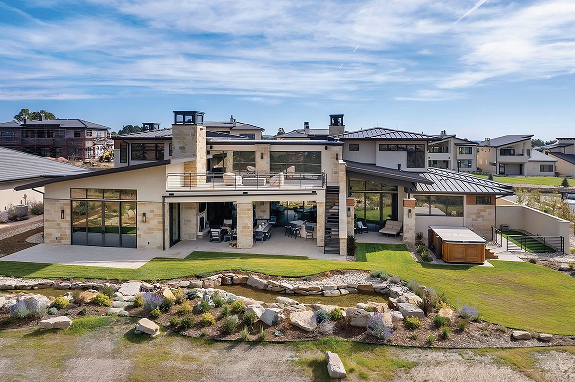 The back view of a modern home with black windows and beautiful landscapes.