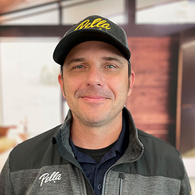 A headshot of a man wearing a Pella baseball cap and wearing a gray Pella jacket.