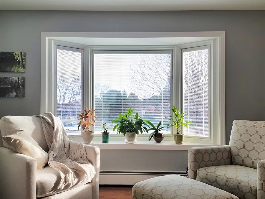 A cozy living room featuring a white bay window with plants, showcasing the after white bow window design.