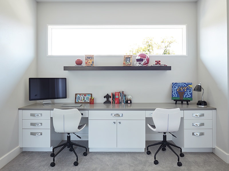 A built-in desk with two chairs is below a wide fixed window